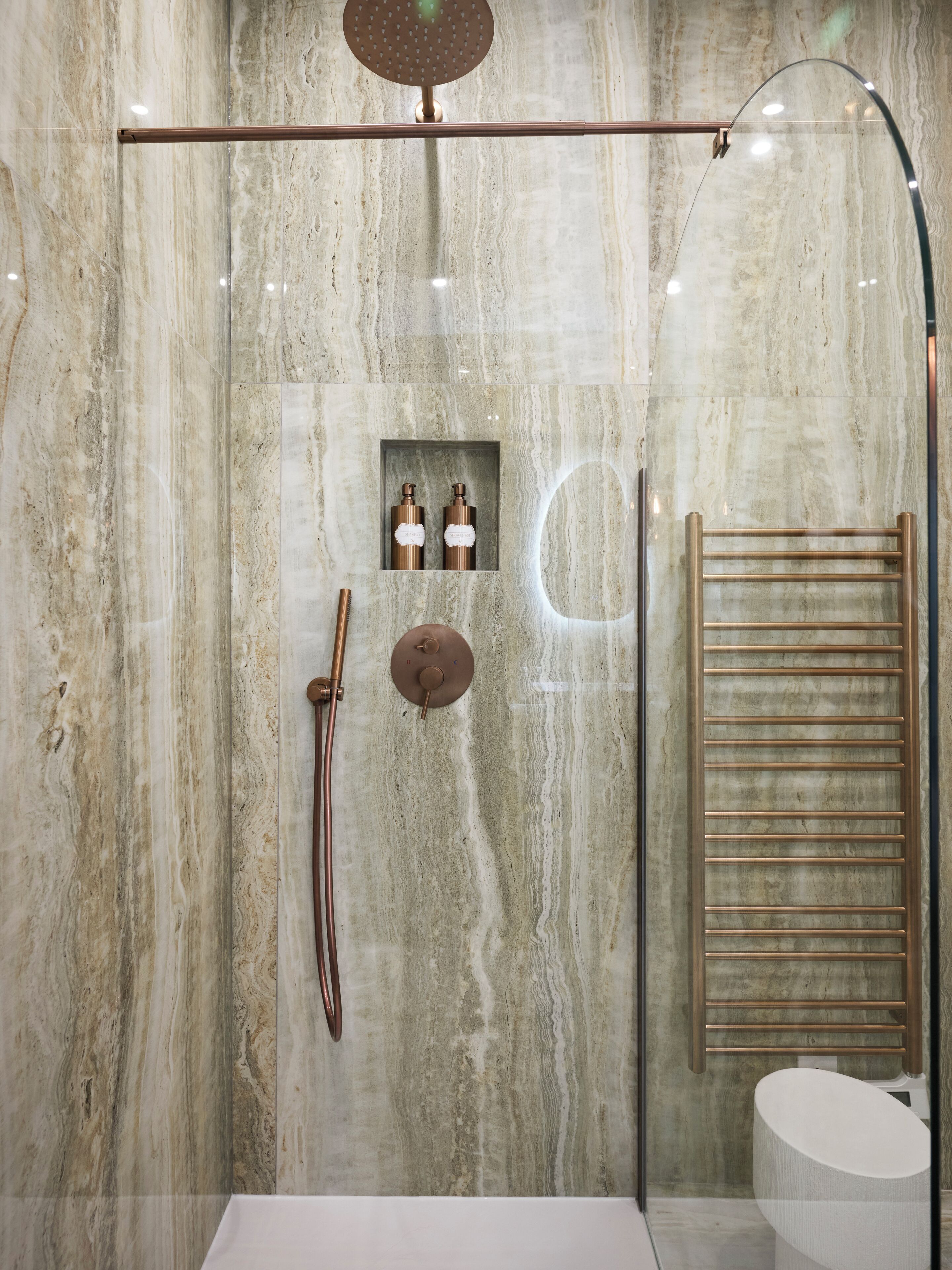 Une douche moderne dotée d’un pommeau de douche à pluie, d’un pommeau de douche à main et d’un distributeur de savon en verre.