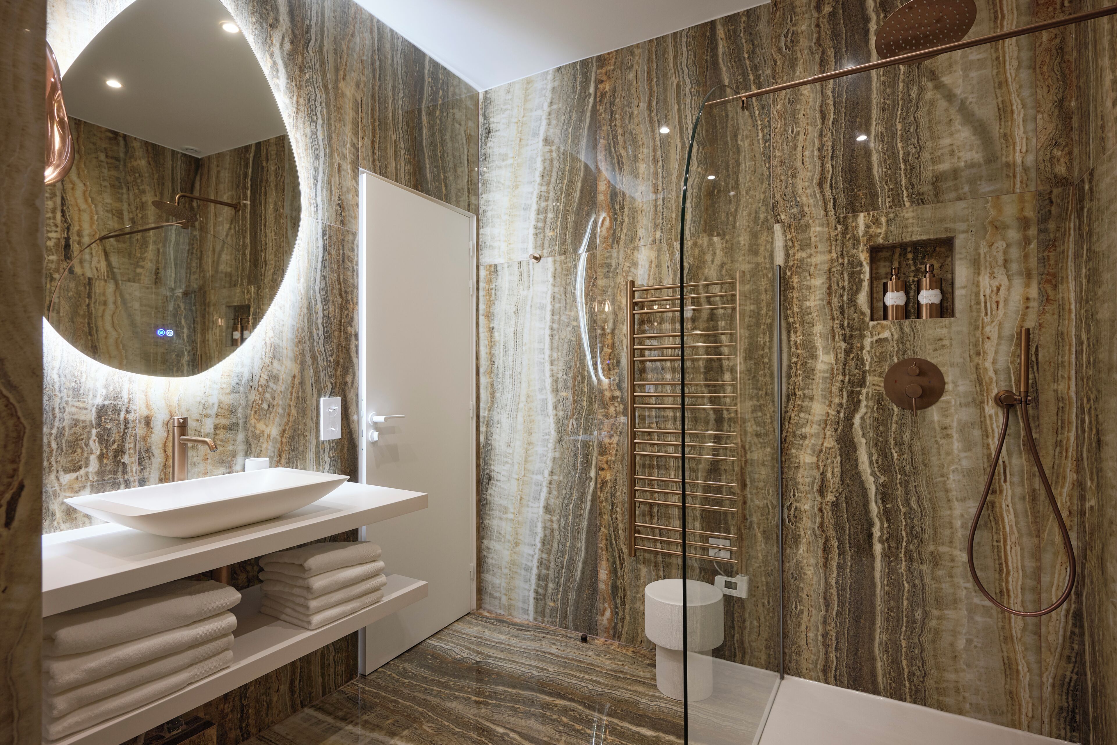 A modern bathroom with a large mirror, a vessel sink, a glass-enclosed shower, and marble walls.