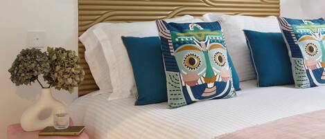 A bedroom with a bed, decorative pillows, a bedside table with a vase, and a wall with a textured pattern.