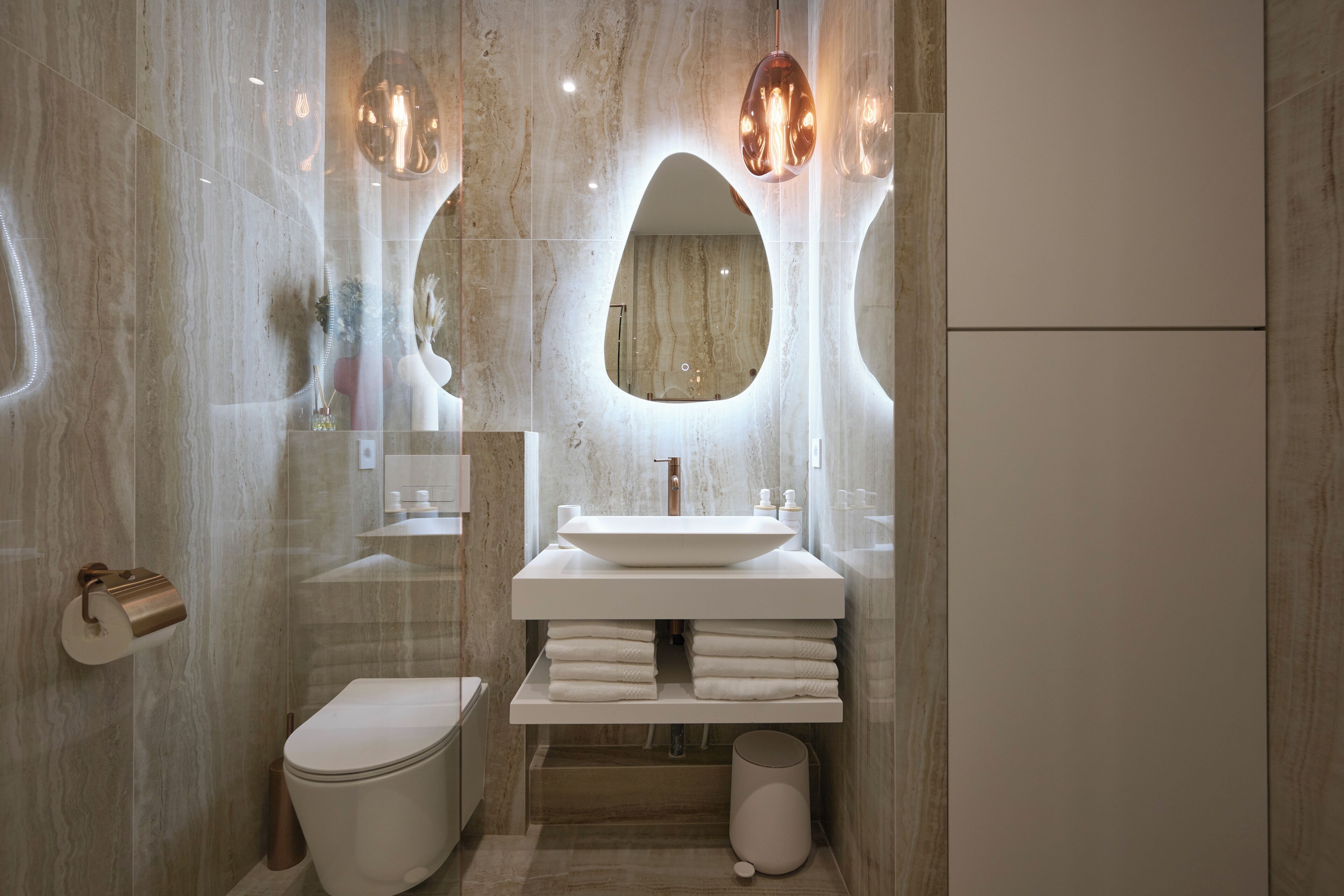 Une salle de bain moderne avec un grand miroir ovale, un lavabo blanc et des toilettes.