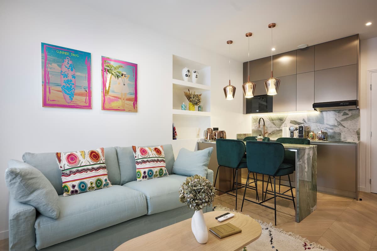 A modern living room with a sofa, a coffee table, and a kitchen area with a marble countertop and pendant lights.