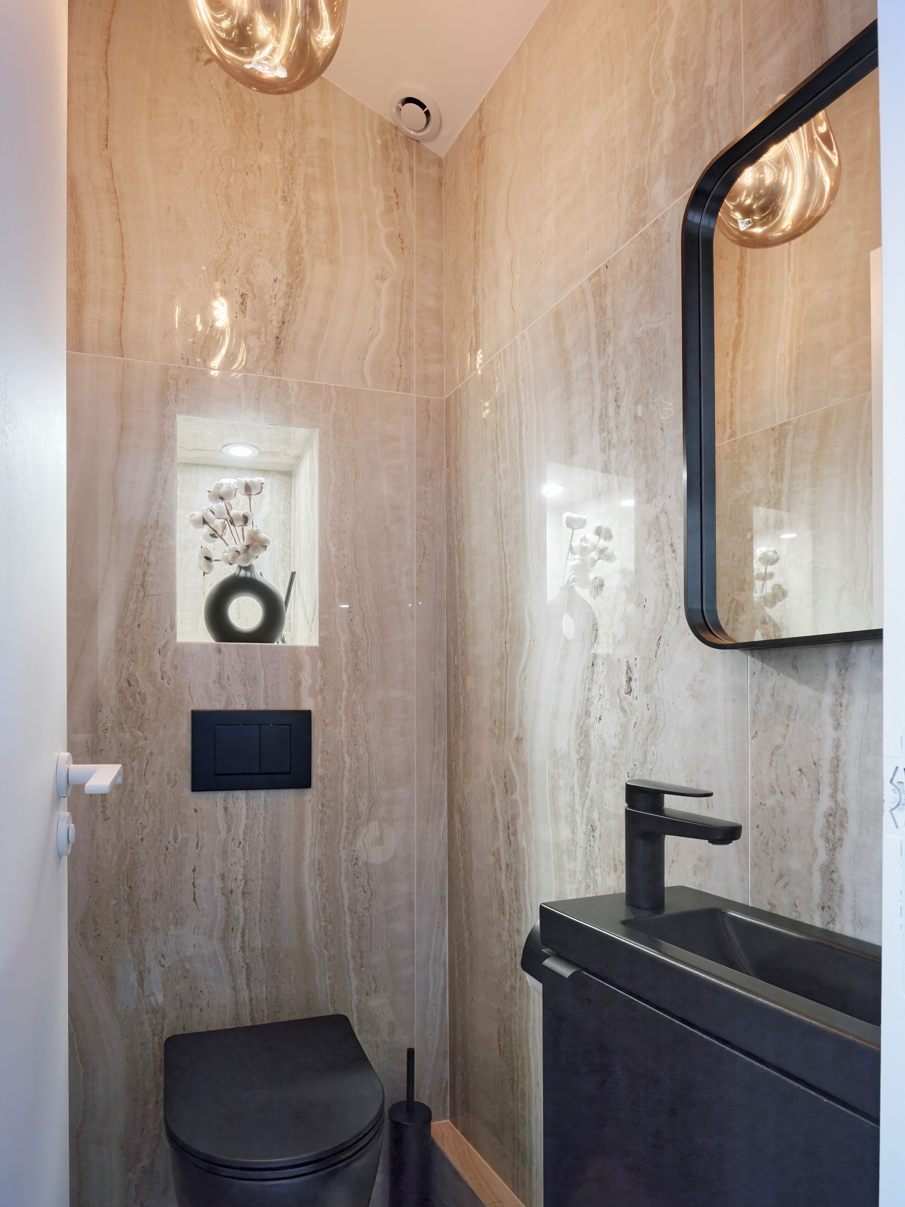 Un baño moderno con pared de mármol, inodoro y lavabo negros, y un espejo.