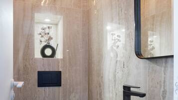 Un baño moderno con pared de mármol, inodoro y lavabo negros, y un espejo.