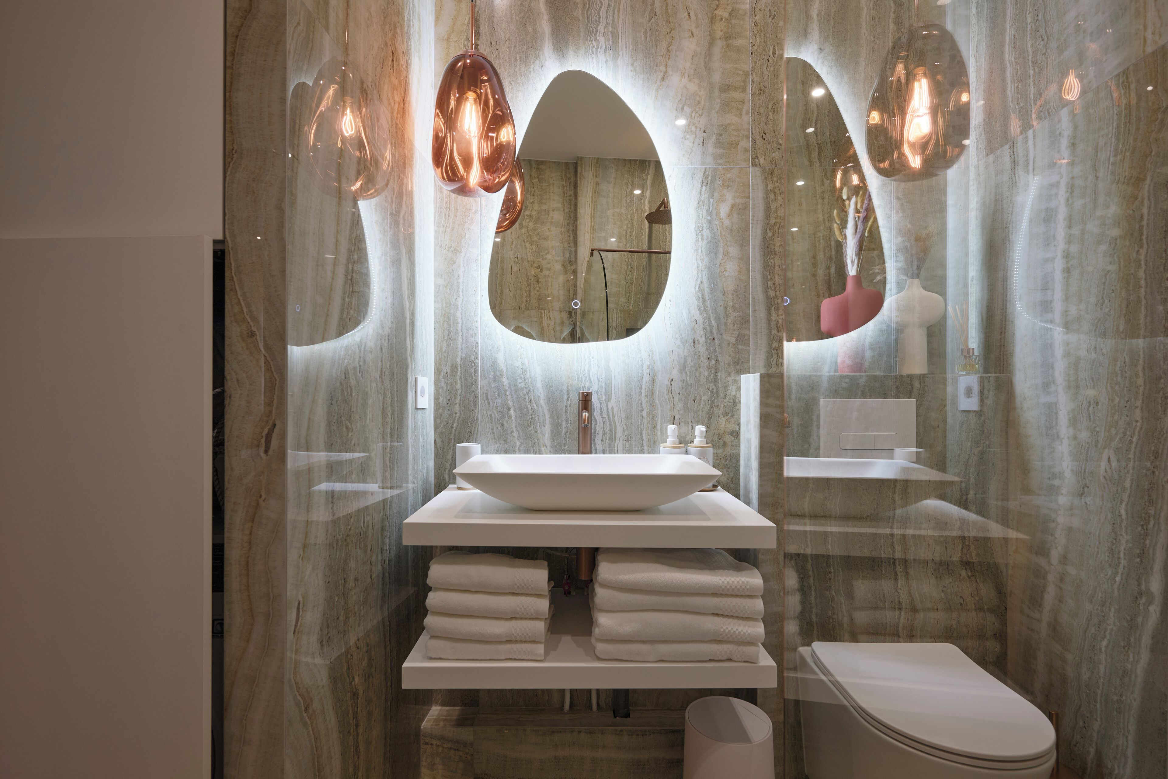 A modern bathroom with a large oval mirror, a white sink, and a toilet.