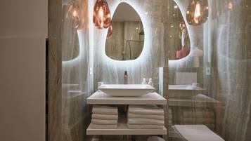 A modern bathroom with a large oval mirror, a white sink, and a toilet.