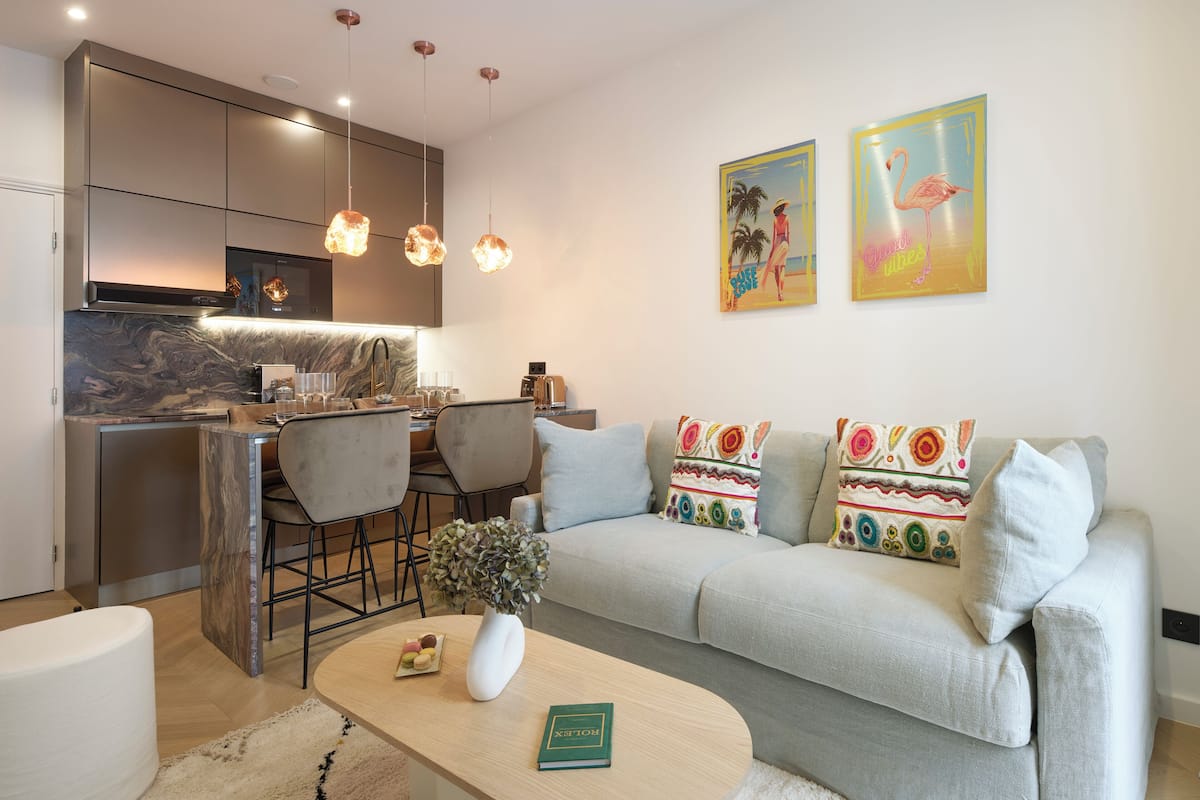 A modern kitchen with a marble countertop, pendant lights, and a dining area with a table and chairs.