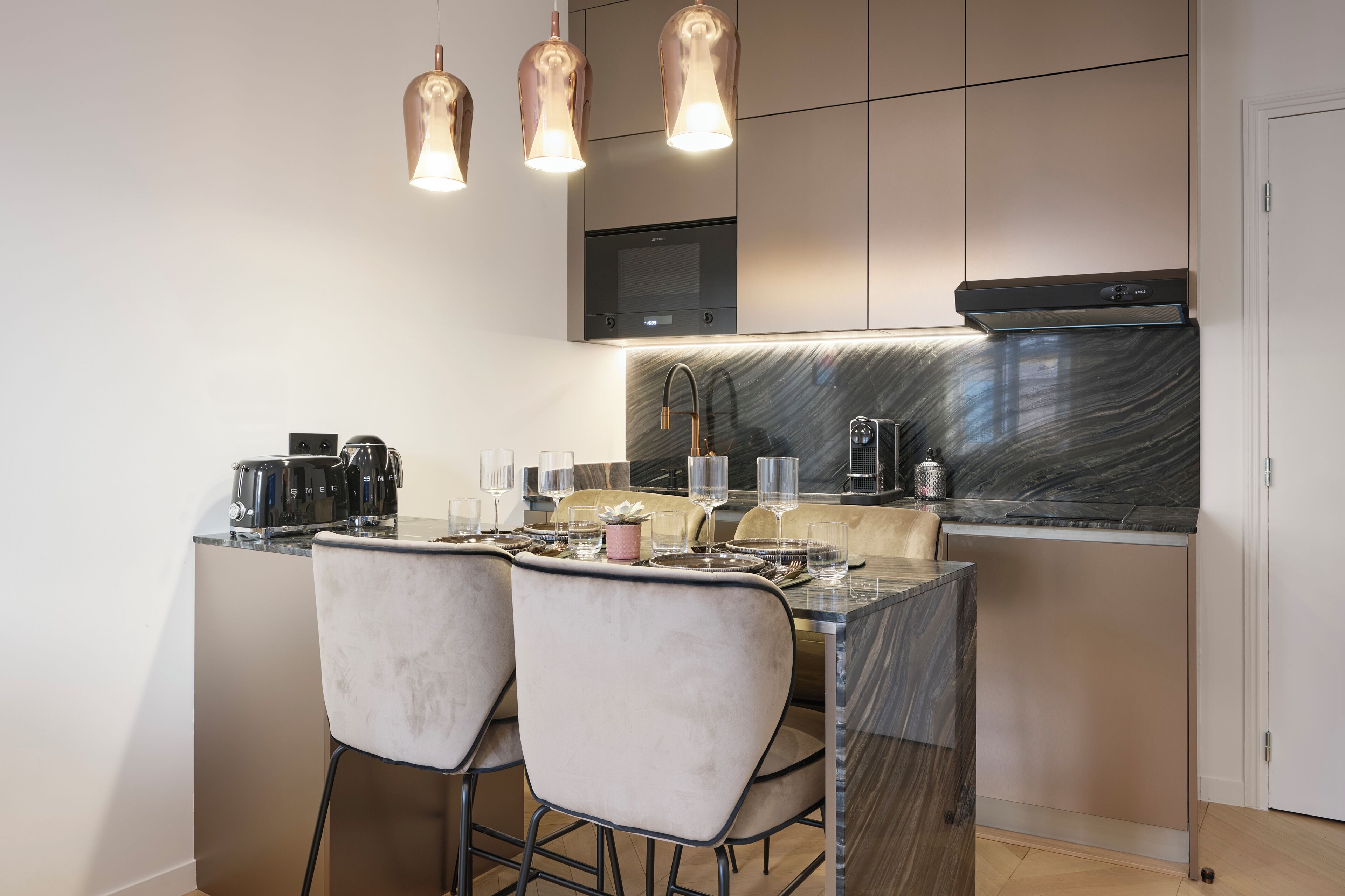 Cuina moderna amb taulell de marbre, electrodomèstics d'acer inoxidable i il·luminació penjant.