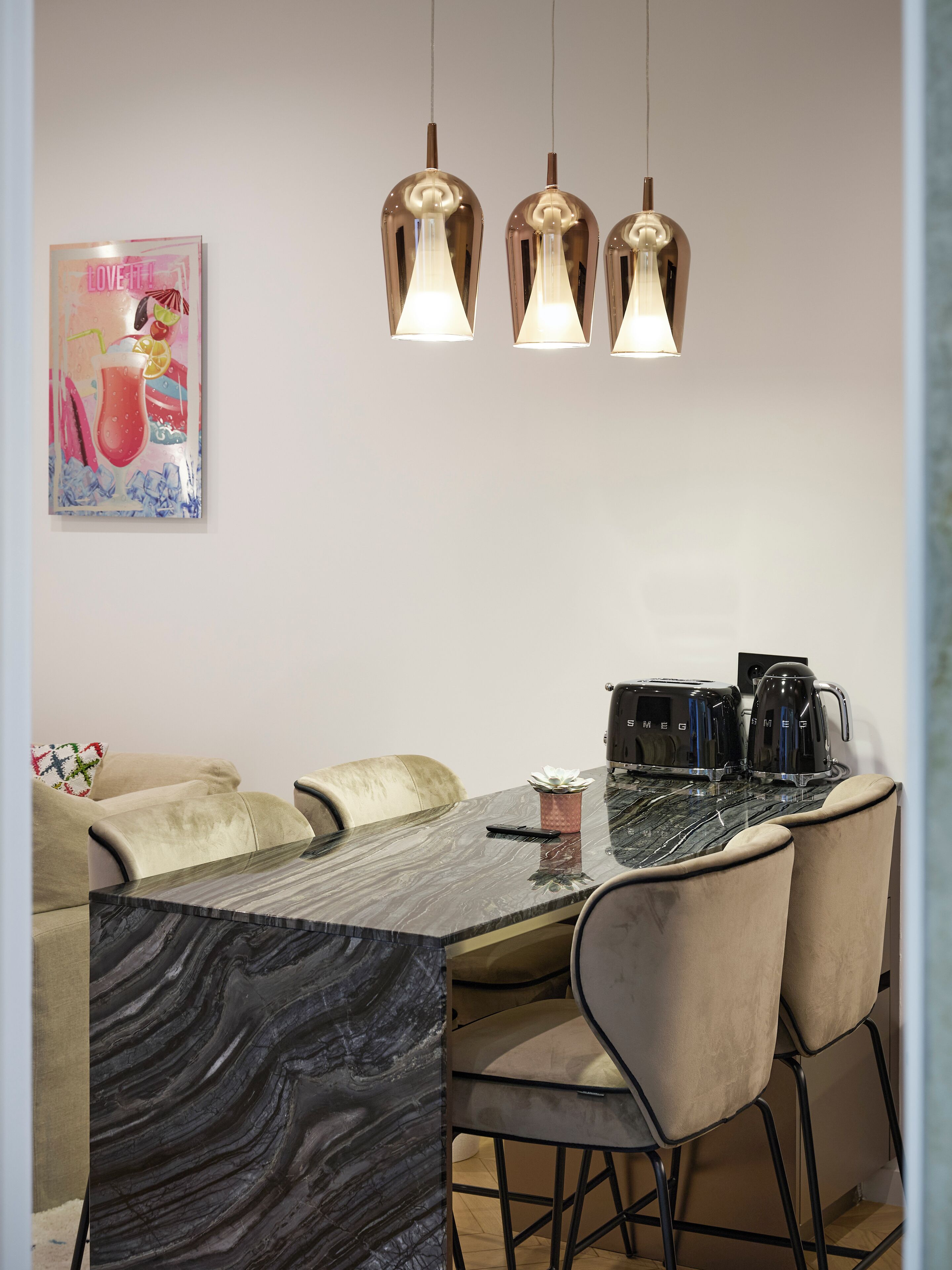 Un espace repas agrémenté d’une table en marbre, de chaises rembourrées et de luminaires suspendus.