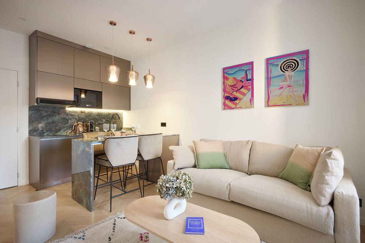 A modern kitchen with a dining area, a sofa, and two artworks on the wall.