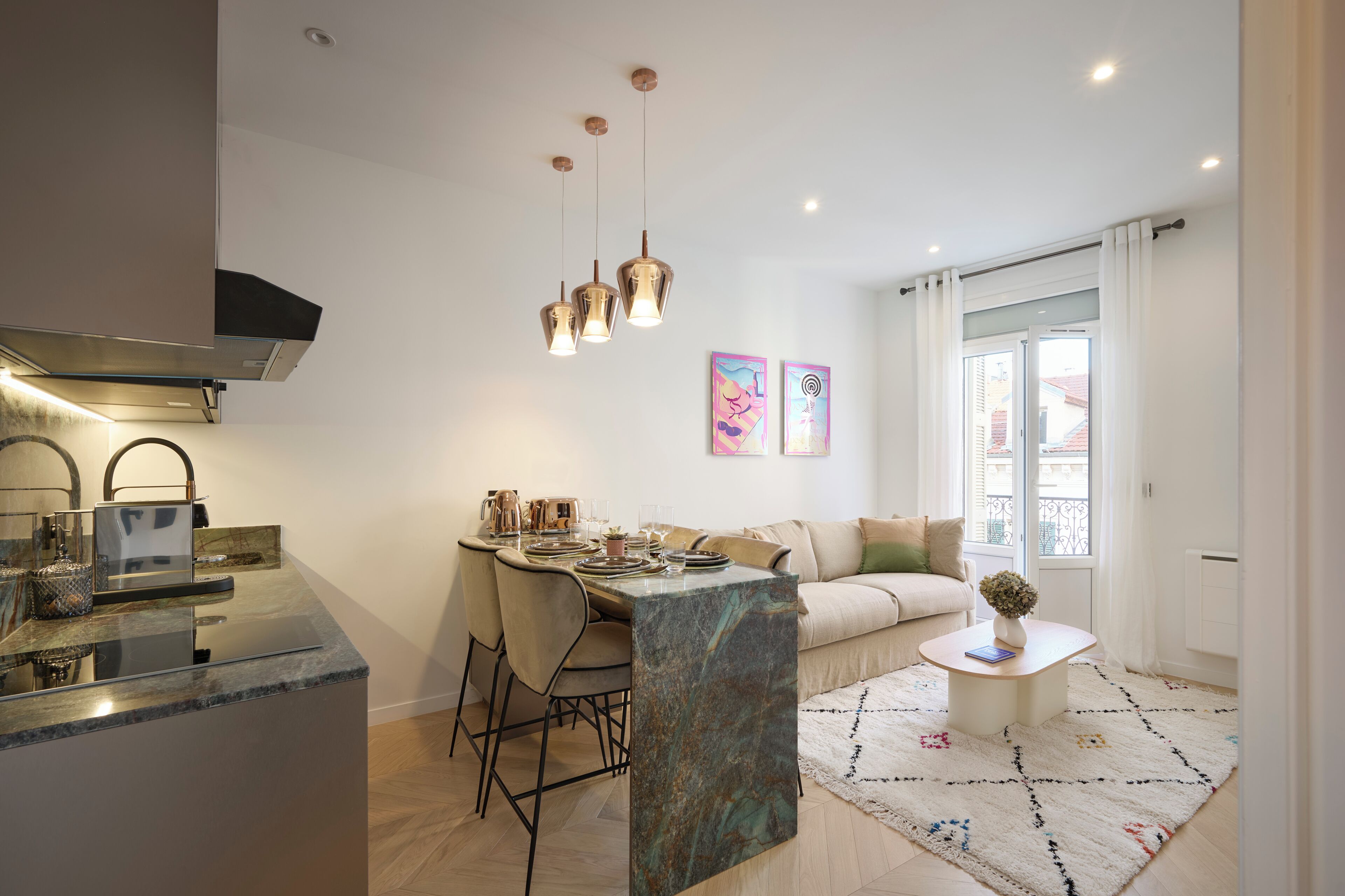 Uma cozinha moderna com ilha de mármore, luminárias pendentes e uma área de refeições com sofá e mesa de centro.