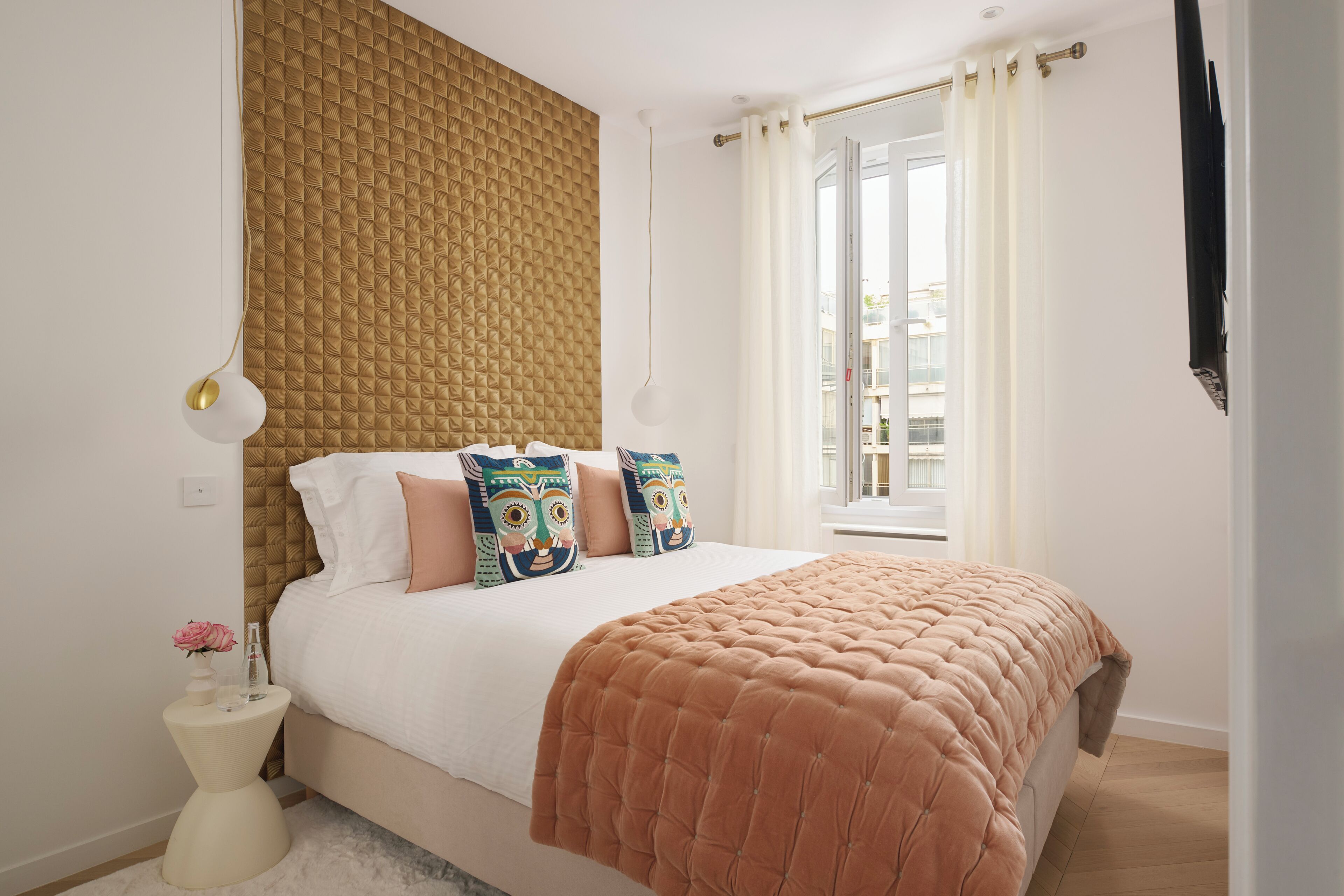 A bedroom with a bed, a nightstand, a window with curtains, and a wall with a textured pattern.