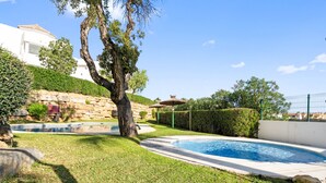 A swimming pool surrounded by a well-maintained lawn, a stone wall, and a large tree. - Apartment 'Sea View Close To The Beach' with Private Pool, Wi-Fi and Air Conditioning (Málaga)