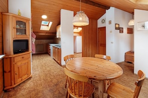 A wooden dining table with chairs, a kitchen area with cabinets, and a ceiling with wooden beams.