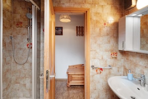 A bathroom with a shower, a sink, and a wooden bench.