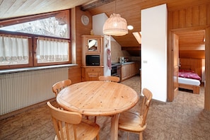 A wooden interior with a round wooden table and chairs, a television, and a bed in the background. - Apartment 'Catinaccio' with Mountain View and Wi-Fi (Soraga di Fassa)