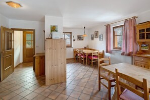 A kitchen with wooden cabinets, a dining table, chairs, and a window with curtains. - Apartment 'Doleda' with Mountain View, Wi-Fi and Air Conditioning (Soraga)