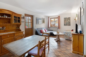 A cozy living room with a dining table, wooden cabinets, a sofa, and a window with curtains. - Apartment 'Doleda' with Mountain View, Wi-Fi and Air Conditioning (Soraga)