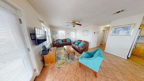 A spacious living room with a brown leather sofa, a teal armchair, and a television on a stand. - Affordable gulfside townhome (Port Saint Joe)