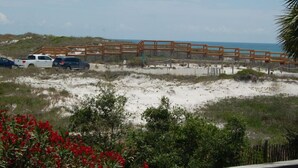 A beach view with a wooden boardwalk, sandy dunes, and parked cars. - Affordable gulfside townhome (Port Saint Joe)