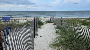 A beach pathway leading to the ocean, with a wooden fence and beach umbrellas.