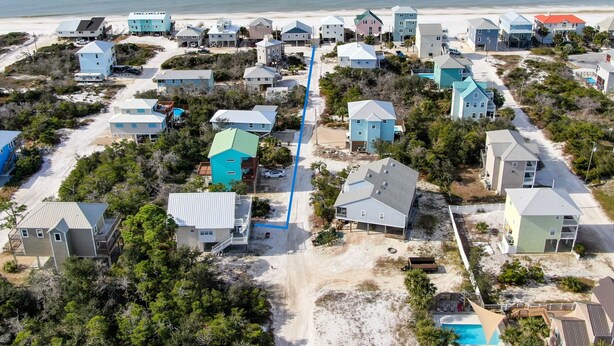 An aerial view of a coastal residential area with houses, a beach, and a swimming pool.