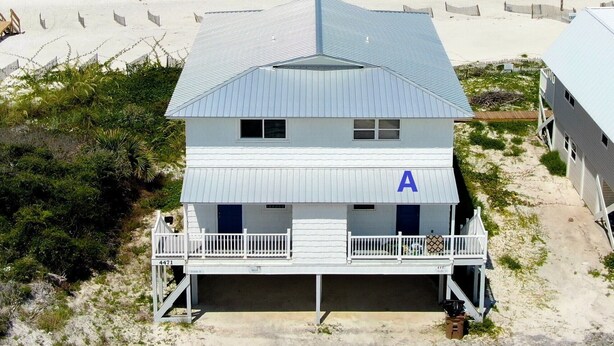 Ein Gebäude direkt am Strand mit einem Metall-Dach, einem Balkon und einem sichtbaren 'A'-Schild an der Seite.