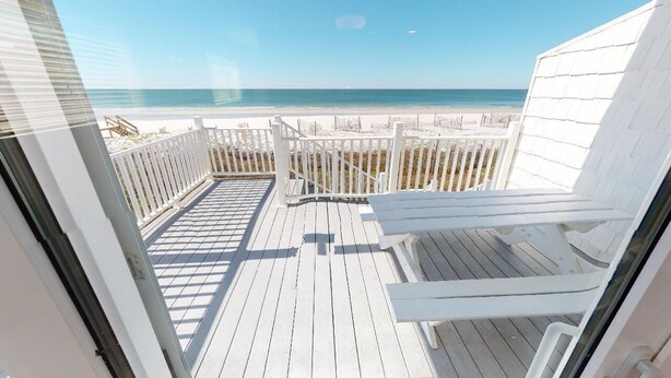 Een houten terras met witte leuningen, een bankje en uitzicht op strand en zee.