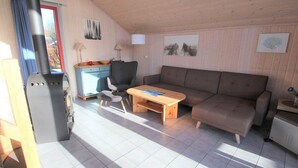 Un salon chaleureux avec un canapé, une table en bois, une chaise, un petit coin cuisine et un poêle à bois.