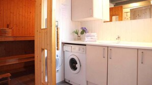 Une petite buanderie aux murs lambrissés, équipée d’un lave-linge, d’un étendoir et d’une petite fenêtre.
