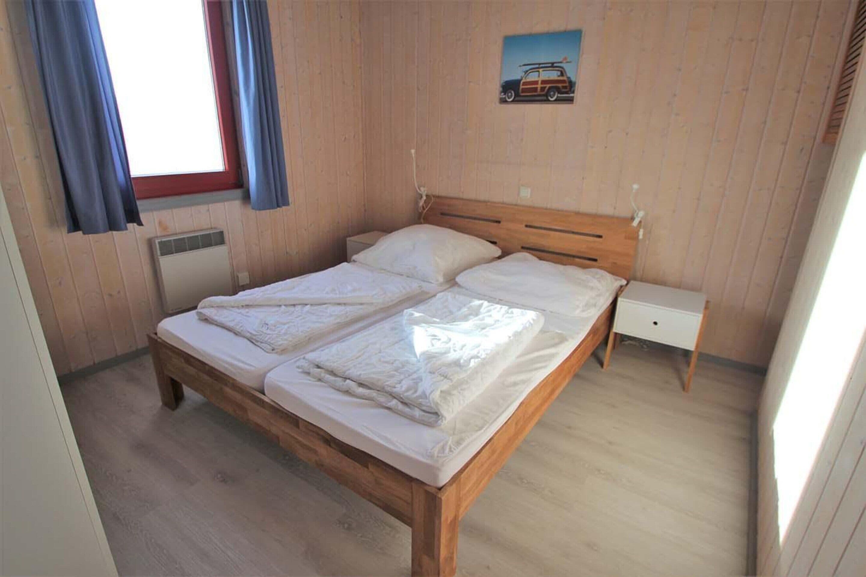 A wooden bed with two pillows and a nightstand in a room with wooden walls and a window with curtains.