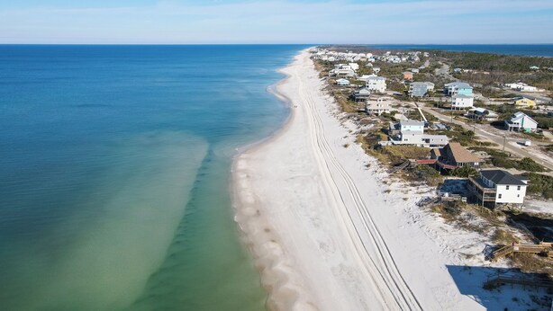 An aerial view of a coastal area with a sandy beach and a row of houses along the shore.