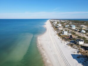 An aerial view of a coastal area with a sandy beach and a row of houses along the shore.