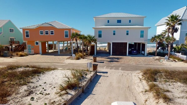 A beachfront property with multiple houses, a sandy driveway, and a clear view of the ocean.