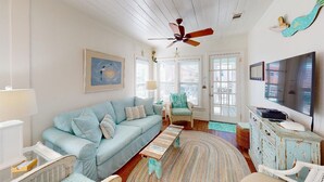 A living room with a light blue sofa, a wooden coffee table, a white wicker chair, a blue armchair, and a television on a white cabinet.