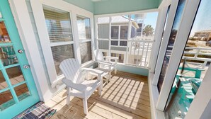 A sunlit room with a wooden floor, white chairs, and a view through large windows.