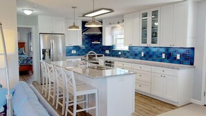 Cozinha moderna com armários brancos, ilha central com banquetas e azulejos azuis na parede.