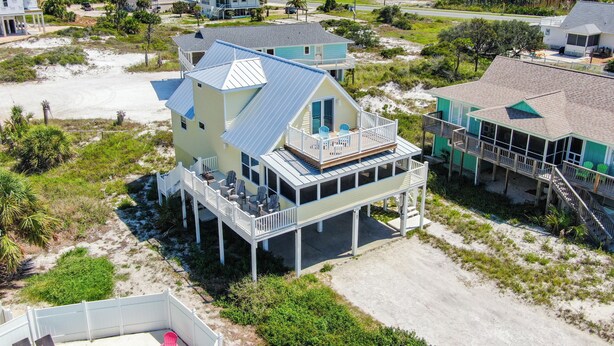 Uma propriedade à beira-mar com uma casa grande, varanda e várias plataformas, cercada por outras casas e uma praia de areia.