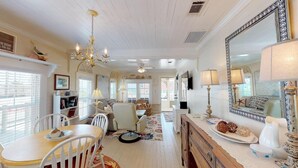 A spacious living room with a chandelier, a dining area with a table and chairs, and a large mirror on the wall. - Gulf View Beach Cottage across from beach access (Port Saint Joe)