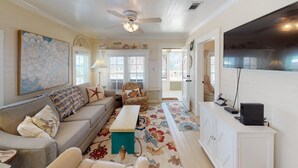 A living room with a sofa, a bench, a television, and a decorative rug. - Gulf View Beach Cottage across from beach access (Port Saint Joe)