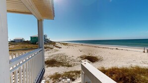 A beach view from a porch with a white railing, a concrete structure, and a green building in the background. - Oceanfront-New furnishing-Steps to Beach (Port Saint Joe)