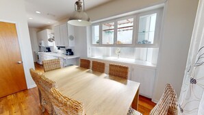 A modern kitchen with white cabinets, a large island, and a dining area with wicker chairs. - Oceanfront-New furnishing-Steps to Beach (Port Saint Joe)