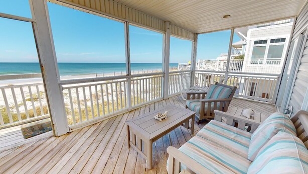 A covered outdoor area with a wooden deck, a sofa, a table, and a view of the beach and ocean. - Oceanfront-New furnishing-Steps to Beach (Port Saint Joe)