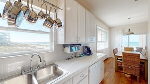 A modern kitchen with white cabinets, stainless steel appliances, and a view of the beach. - Oceanfront-New furnishing-Steps to Beach (Port Saint Joe)
