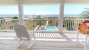 Une terrasse en bois avec une chaise blanche, une piscine et une vue sur la plage.