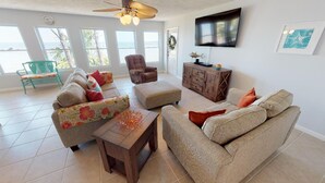 A spacious living room with a sofa, ottoman, and armchair, a wooden cabinet, and a television on the wall. - Bayfront Home near Salinas Park and Pickleball (Port Saint Joe)