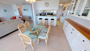 A modern kitchen with white cabinets, a central island with stools, and a dining area with wicker chairs and a glass table. - Bayfront Home near Salinas Park and Pickleball (Port Saint Joe)