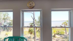 A room with three windows overlooking a beach, a clock on the wall, and a teal chair. - Bayfront Home near Salinas Park and Pickleball (Port Saint Joe)