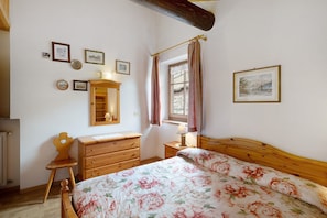 Une chambre à coucher avec un lit en bois, une commode, un miroir et une fenêtre avec des rideaux.