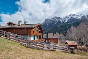 Un chalet en bois doté d’un toit à pente, d’un escalier en bois et offrant une vue sur des montagnes enneigées.