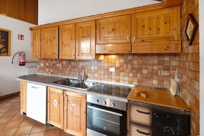 Een keuken met houten kastjes, een roestvrijstalen spoelbak, een betegelde achterwand en een inbouwoven.